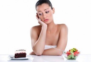 Young woman choosing between cake and healthy salad